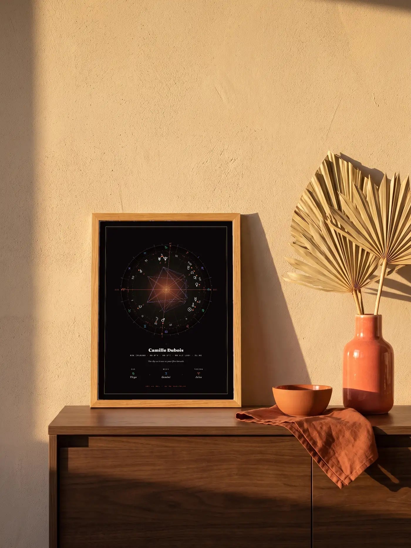 A small oak-tone framed Natal Blueprint in the Element style leans on a walnut sideboard beside a coral vase in golden-hour light.